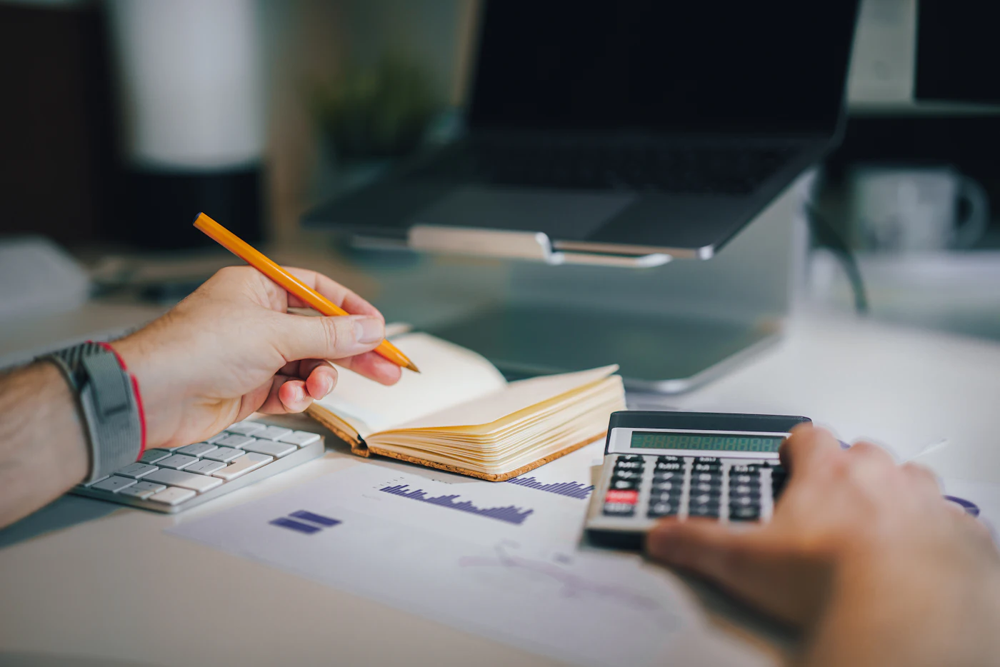 Hands working with a notebook and a calculator at a desk.